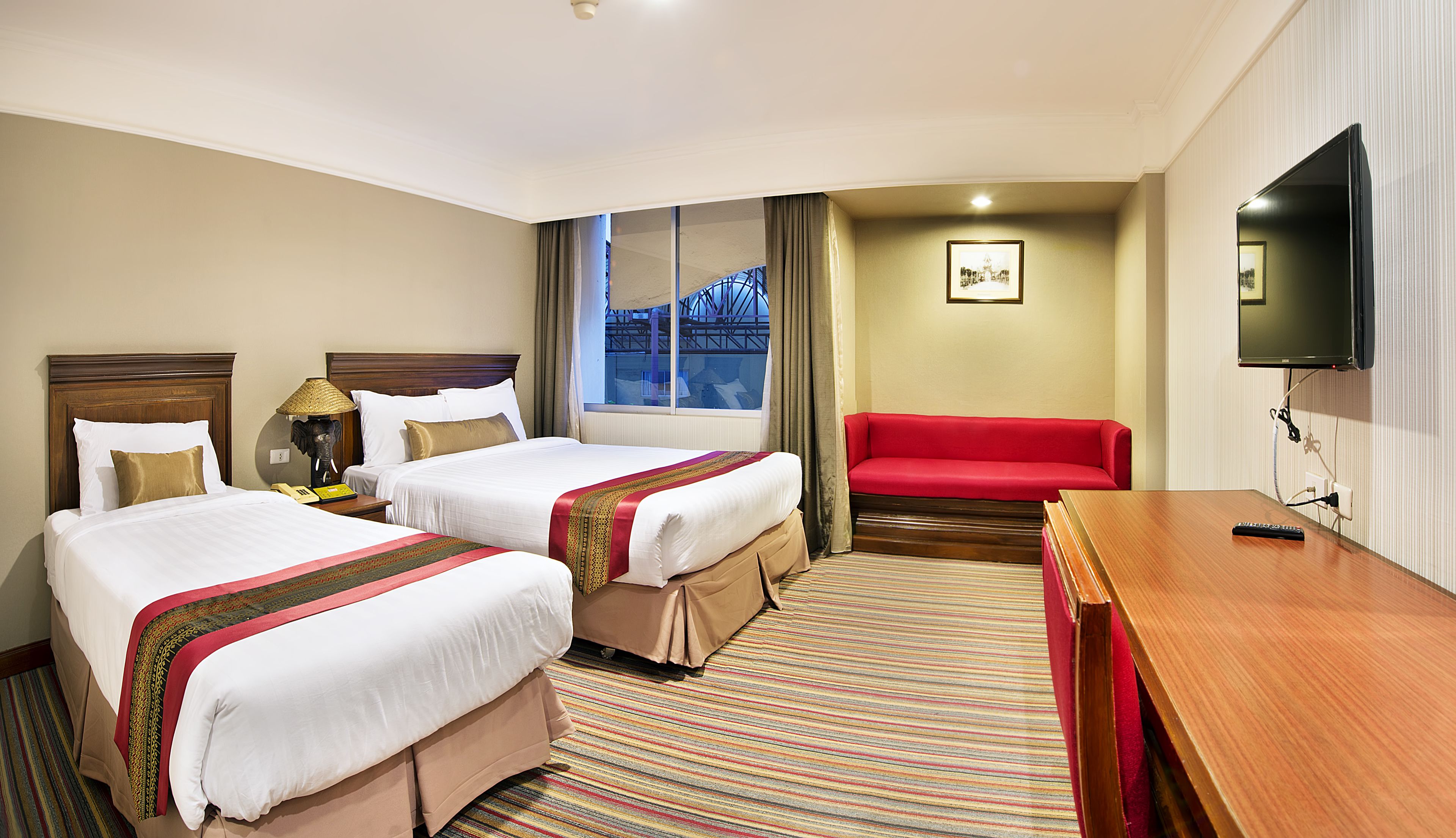 A hotel room with two beds, a red sofa, a TV, and a window with curtains.