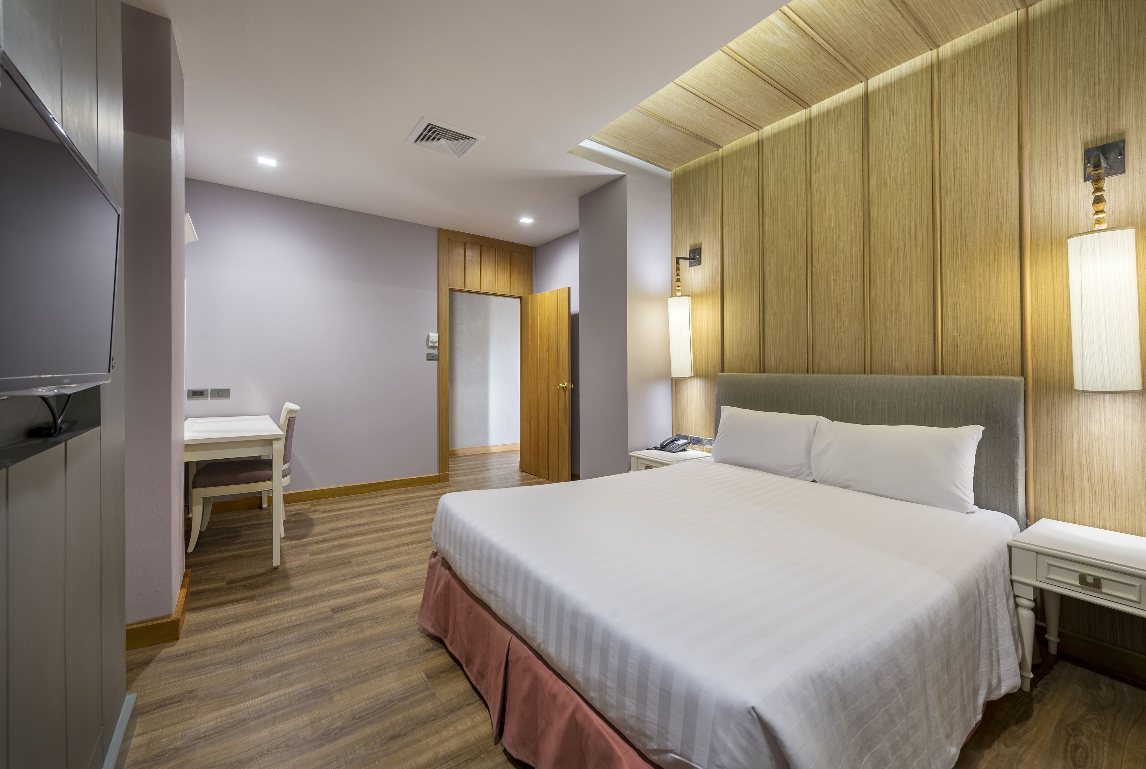 A hotel room with a large bed, a desk, a chair, and a wardrobe.