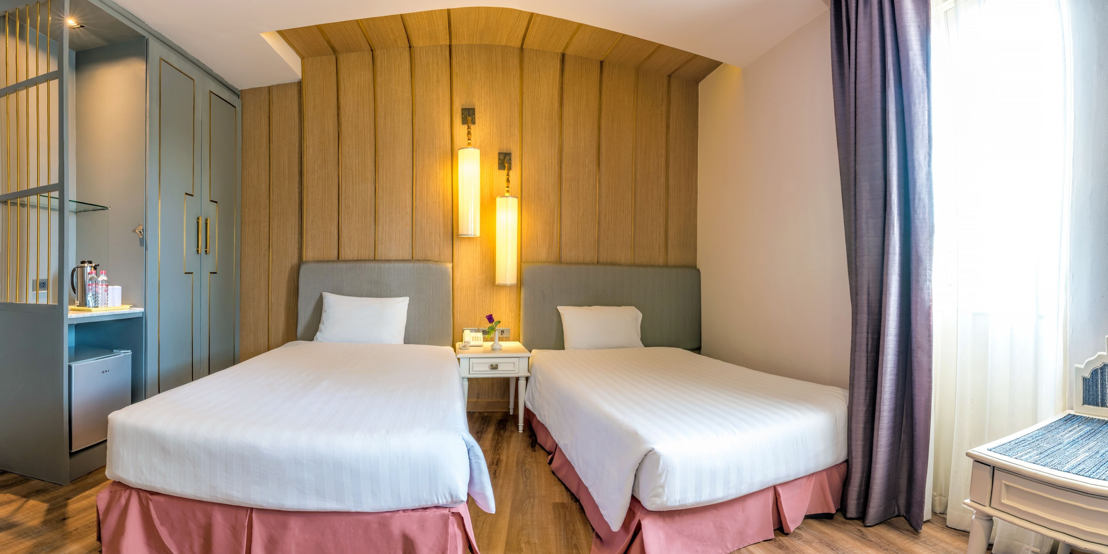 A hotel room with two beds, a small table, a nightstand, and a wardrobe.