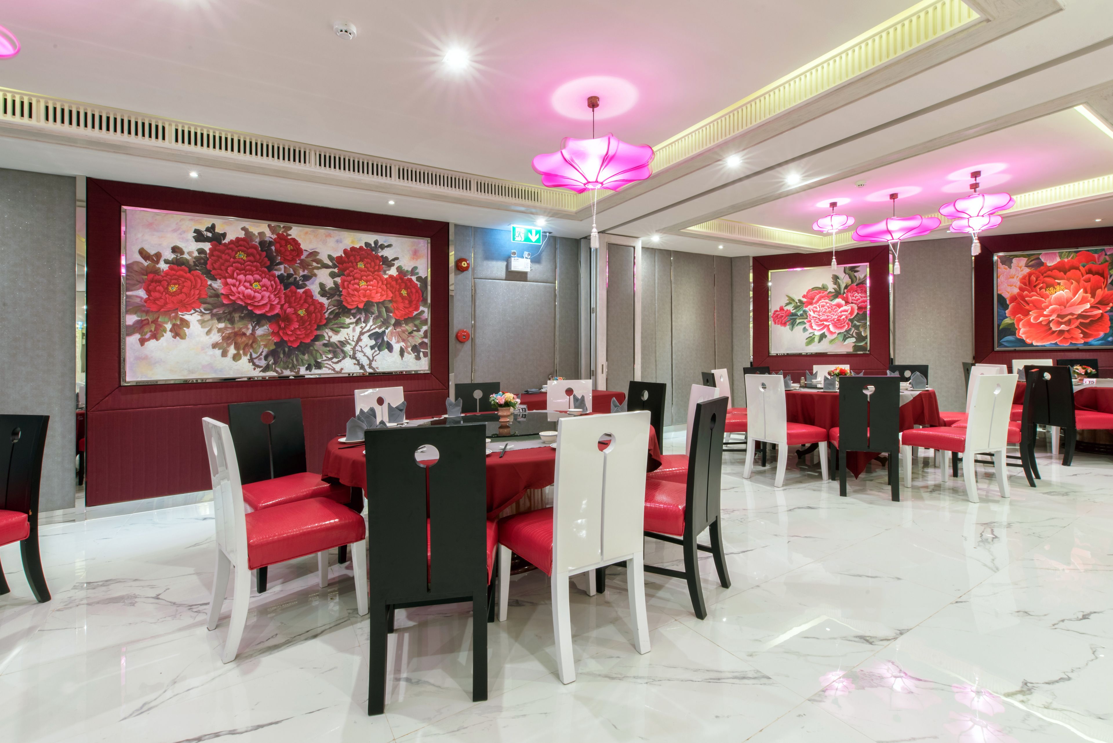 A dining area with red chairs and tables, large floral paintings on the walls, and a modern ceiling design.