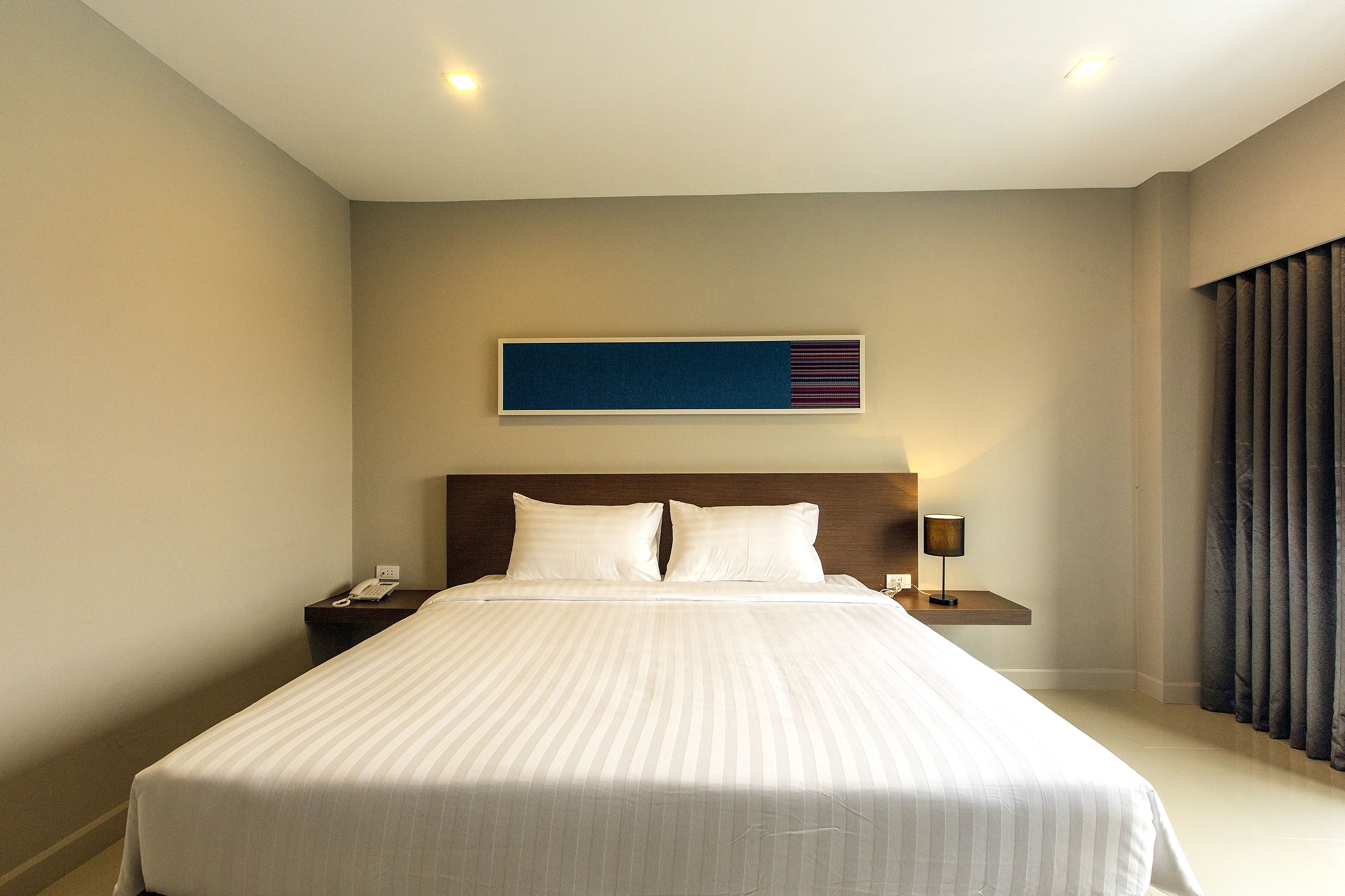 A hotel room with a large bed, a nightstand, a lamp, and a wall-mounted artwork.