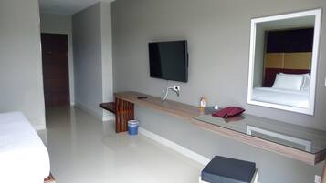 A modern hotel room with a bed, a desk with a flat-screen TV, a mirror, and a small stool.