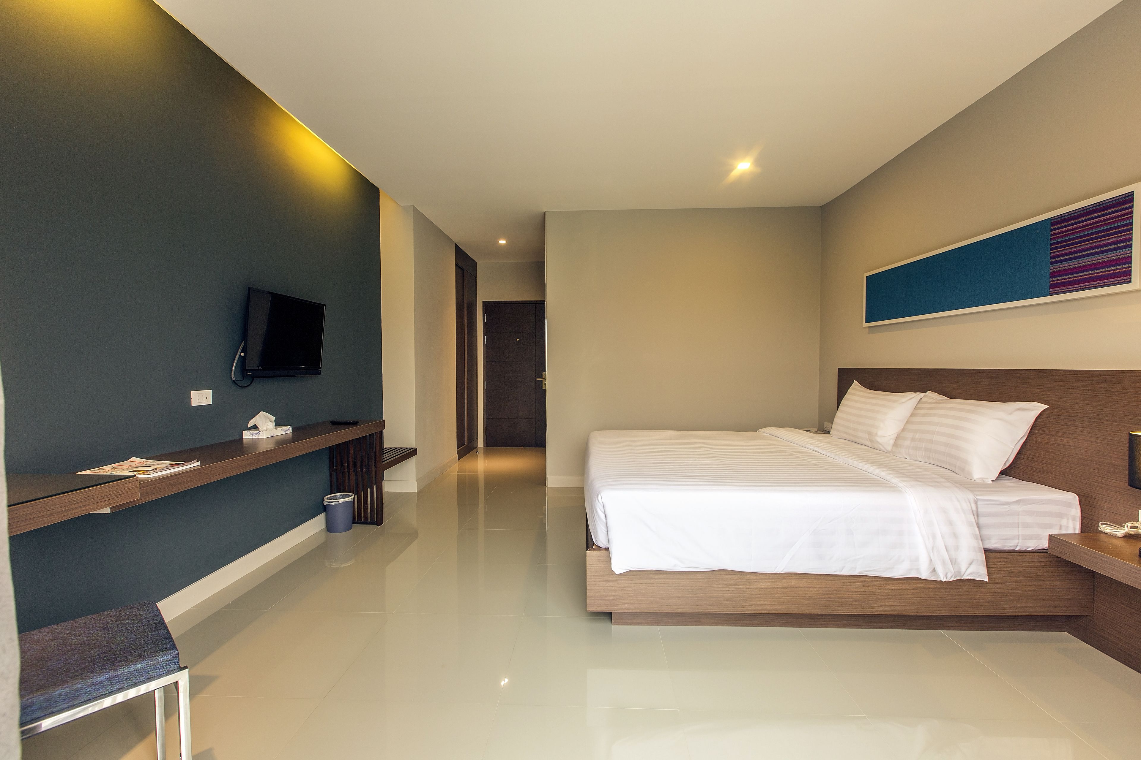 A modern hotel room with a large bed, a desk, a flat-screen TV, and a minimalist design.