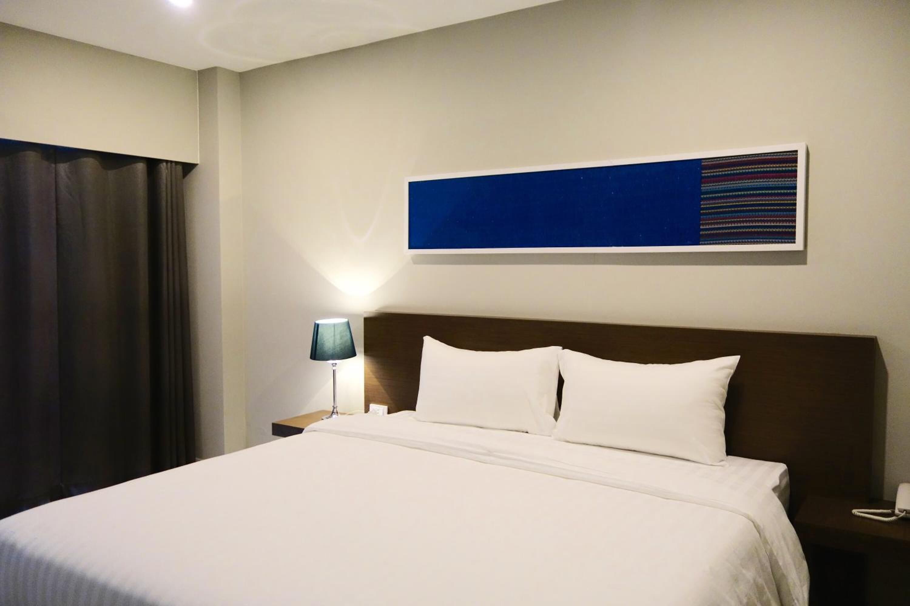 Una habitación de hotel con una cama grande, una mesita de noche con una lámpara y una obra de arte colgada en la pared.