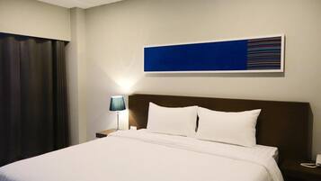 Una habitación de hotel con una cama grande, una mesita de noche con una lámpara y una obra de arte colgada en la pared.
