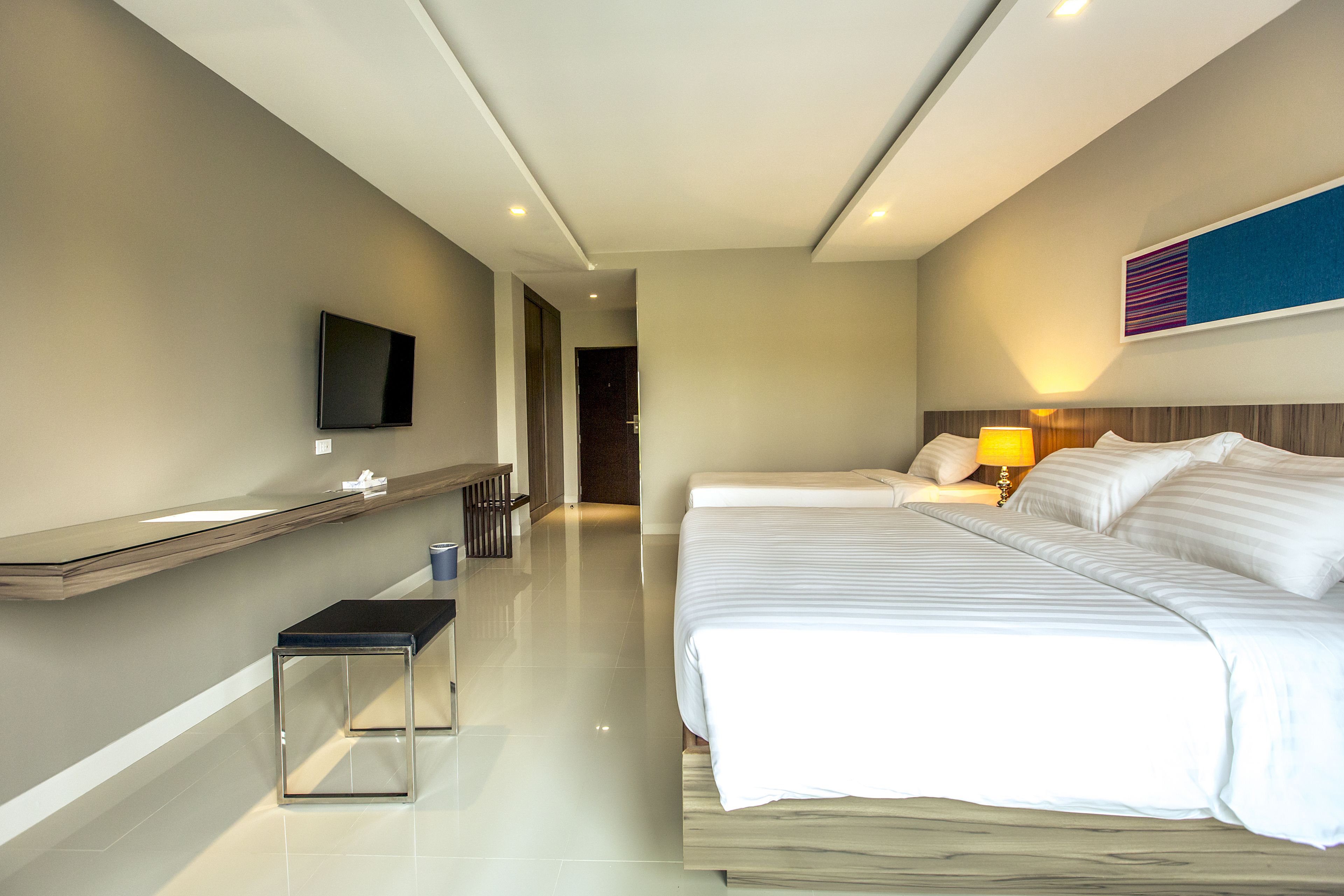 Une chambre d’hôtel moderne dotée d’un grand lit, de tables de chevet, d’un téléviseur à écran plat et d’une salle de bain visible à travers une porte ouverte.