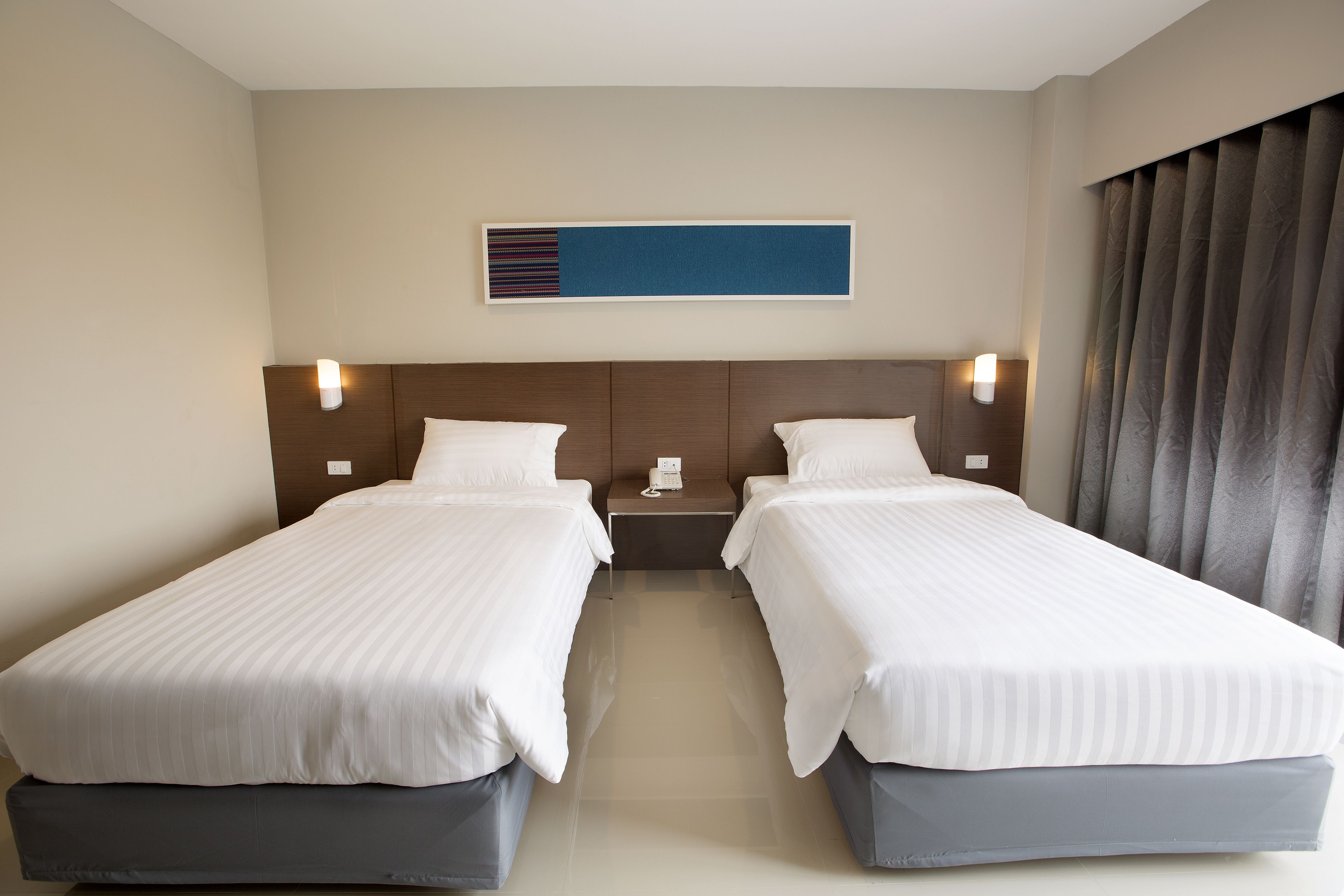A hotel room with two single beds, a nightstand with a phone, and a wall-mounted light fixture.