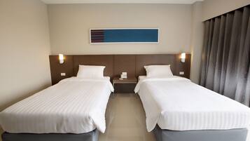 A hotel room with two single beds, a nightstand with a phone, and a wall-mounted light fixture.
