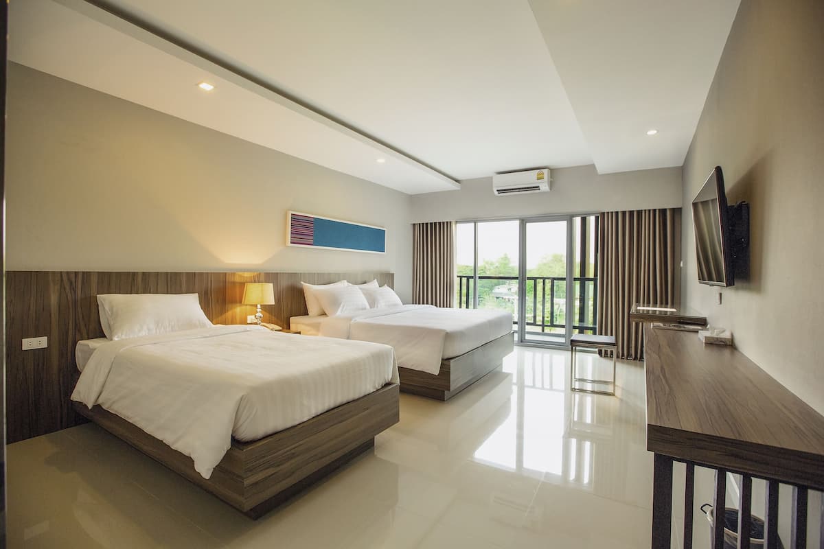 Habitación de hotel moderna con dos camas, televisión y balcón con cortinas.