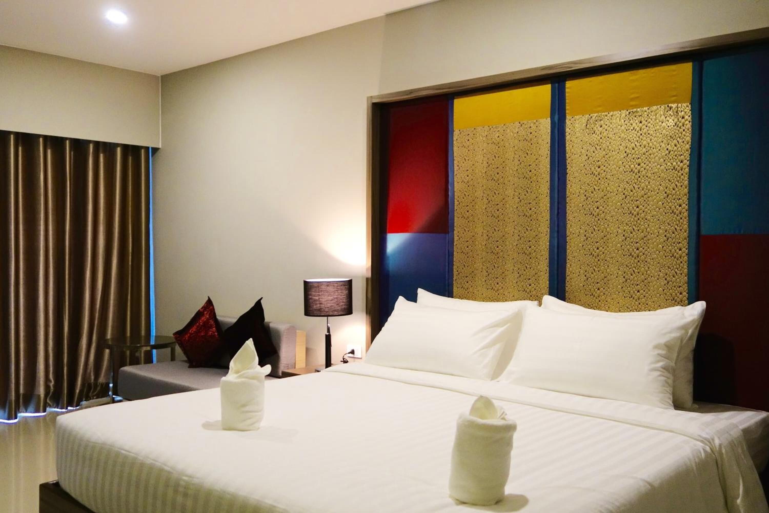 Habitación de hotel con una cama grande, una mesita de noche con lámpara y vistas a la ciudad a través de la ventana.