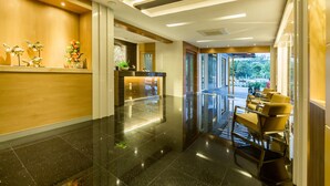 A hotel reception area with a polished black floor, wooden reception desk, and seating area with chairs.