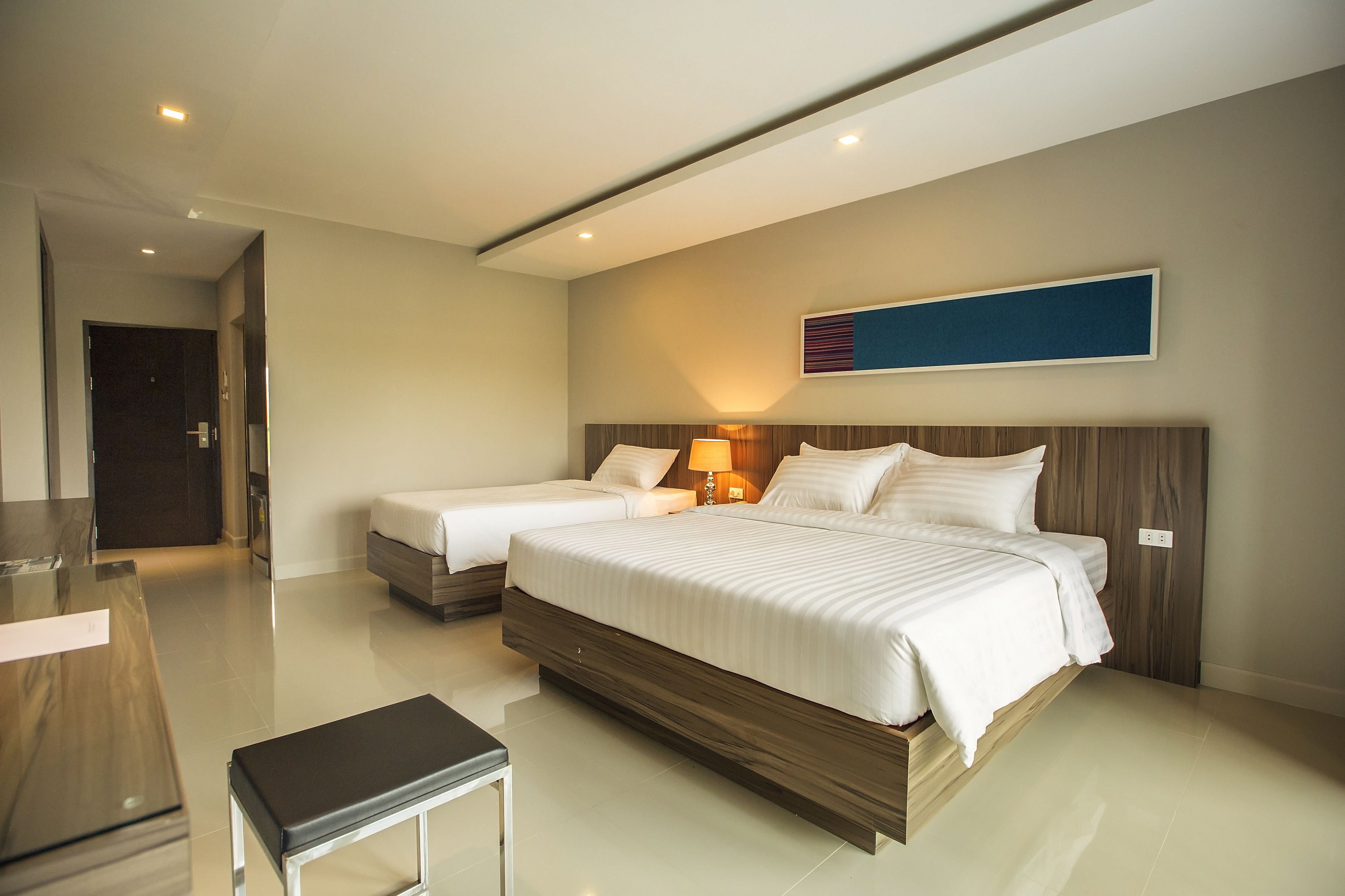 Una habitación de hotel con una cama grande, una cama más pequeña, un escritorio y un banco.