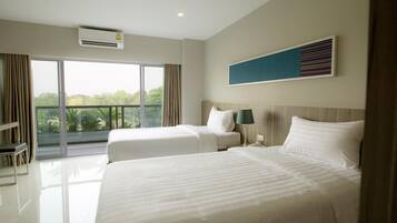 A hotel room with two beds, a large window, and a view of greenery.