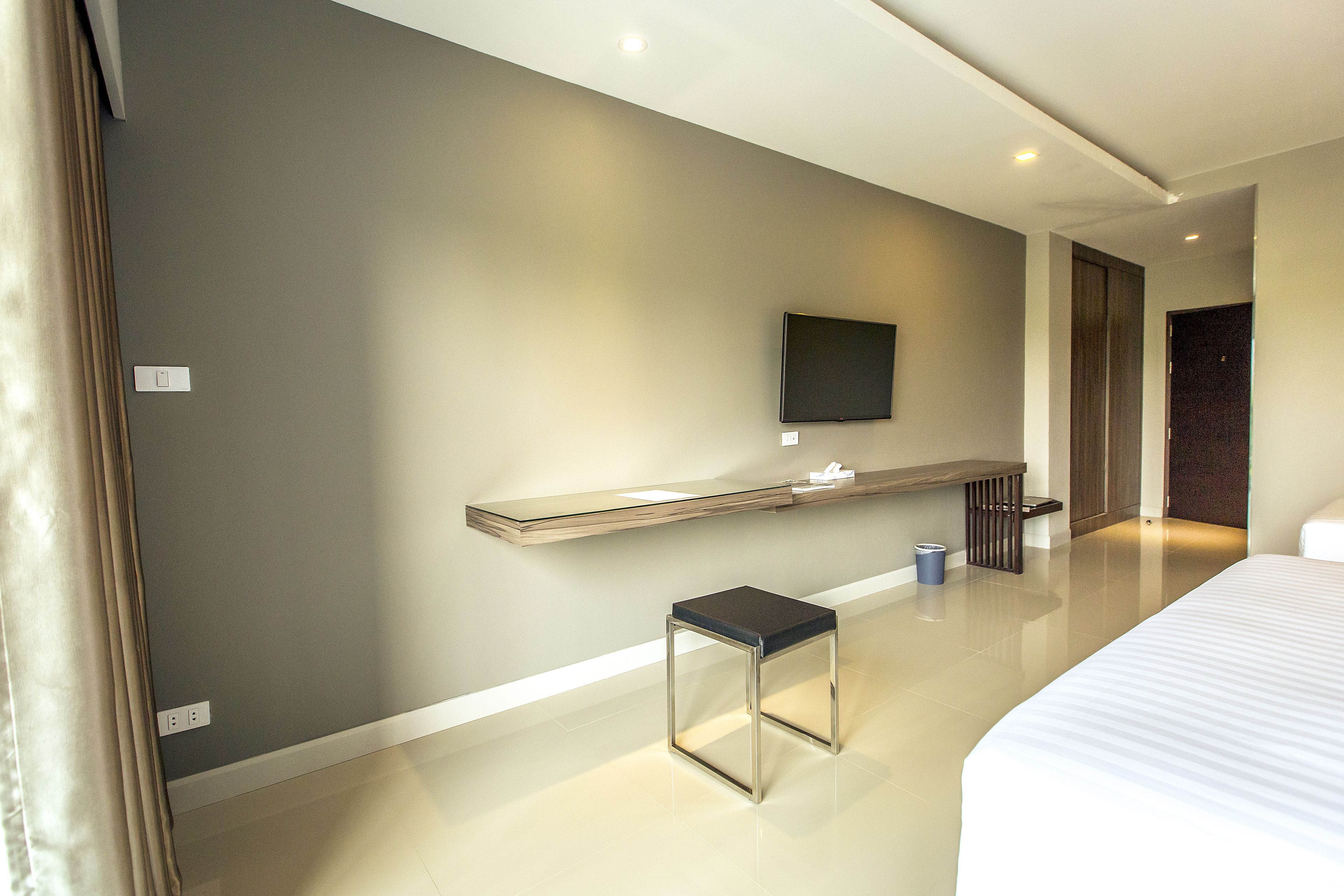 A modern hotel room with a large bed, a small table, a flat-screen TV mounted on the wall, and a minimalist design.