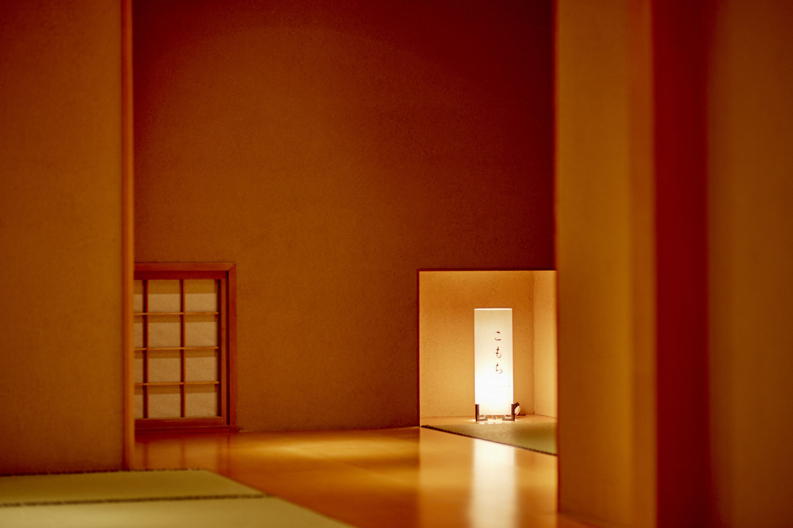 Een minimalistisch ingerichte kamer met een schuifdeur, een klein raam en een lichtbron in de verte.
