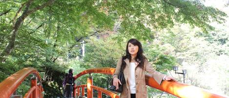 A person standing on a bridge with orange railings, surrounded by greenery.