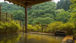 A serene outdoor hot spring area with a wooden deck, a small seating area, and lush greenery in the background. - Fukuichi (Shibukawa)