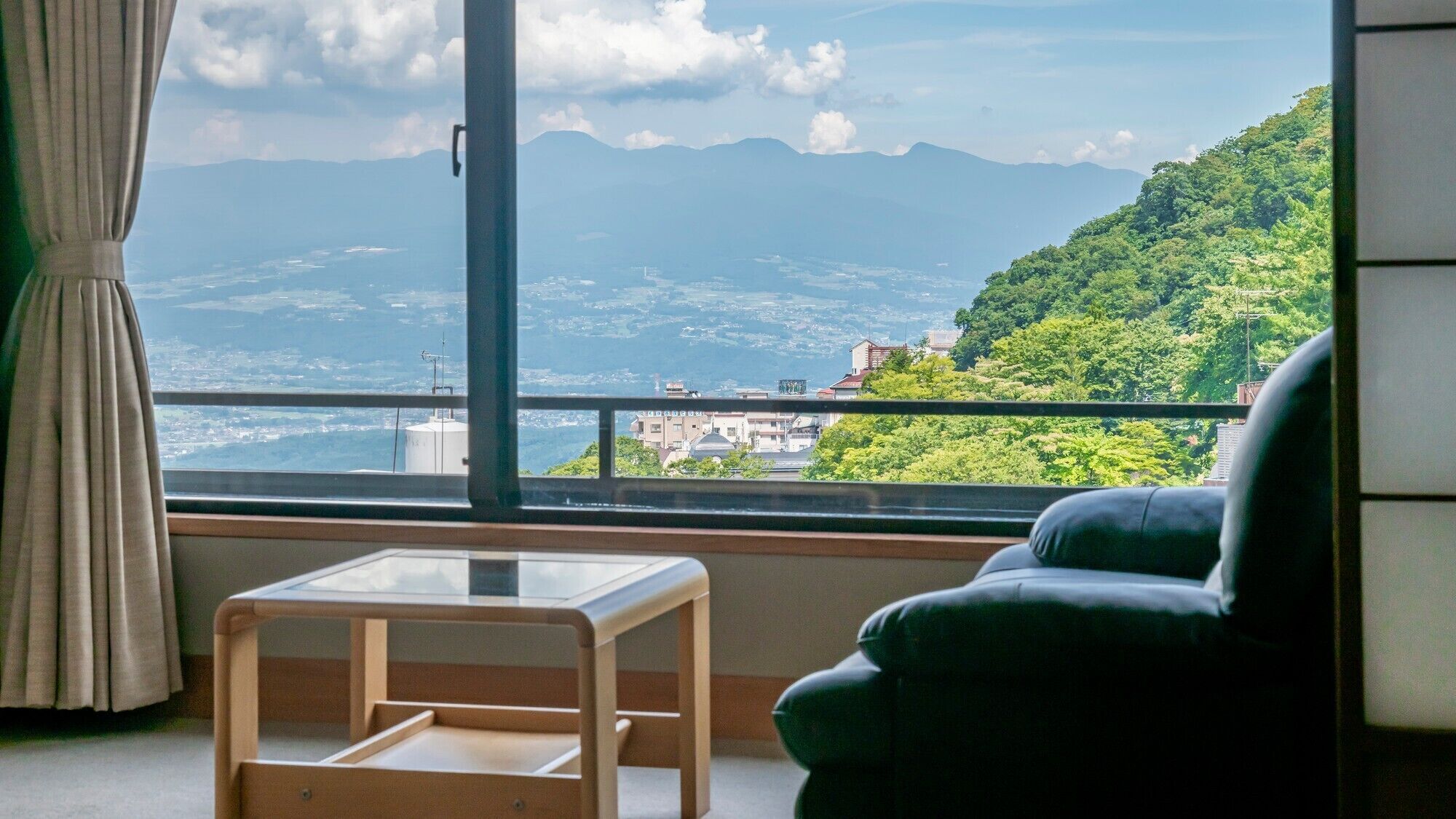 Una habitación con vista a un paisaje montañoso, un balcón con barandilla, una silla y una mesita.