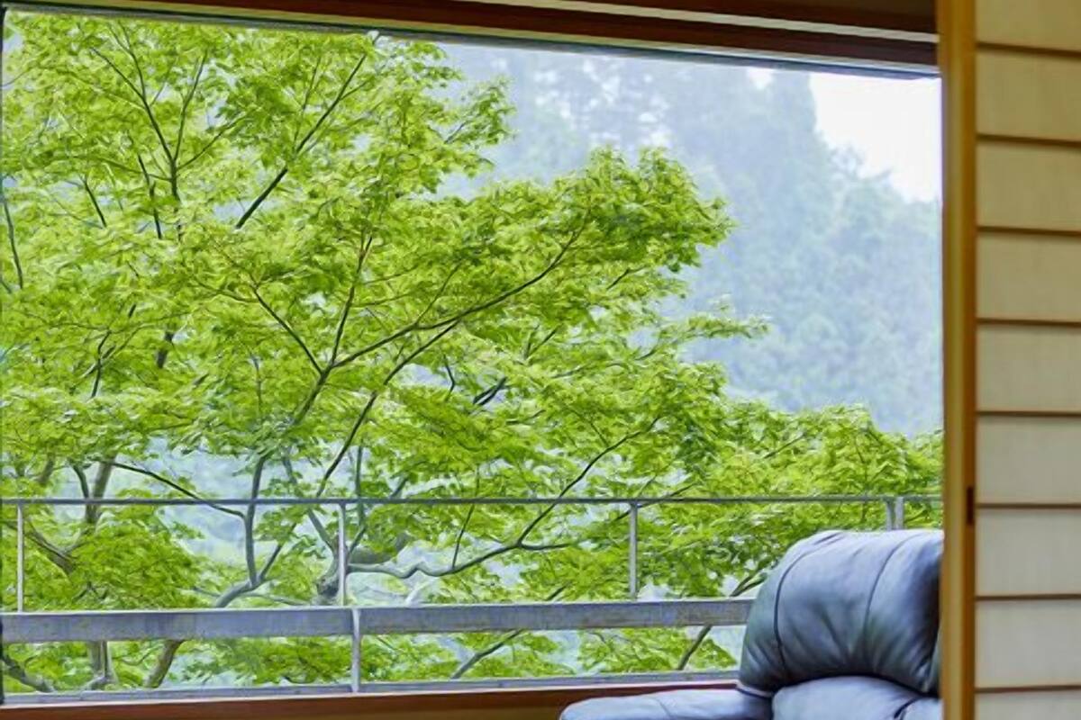 A room with a large window, a glass table, a leather sofa, and a wooden floor.