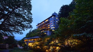 A multi-story hotel nestled among trees with illuminated windows and a visible outdoor area. - Fukuichi (Shibukawa)