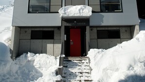 A modern building with a red door, surrounded by snow. - Powder Haven (Kutchan)