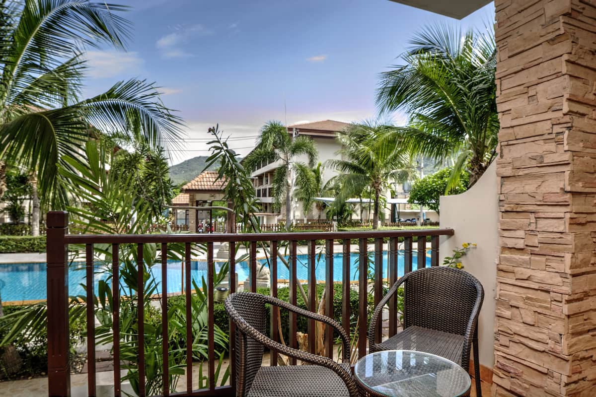 Ein Balkon mit Korbstühlen und einem Glastisch mit Blick auf einen Swimmingpool und ein Resortgebäude.