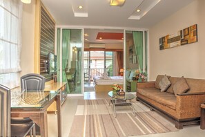 A modern living room with a glass dining table, a wicker sofa, and a bed with a view to the outside. - Whispering Palms Suite (Koh Samui)