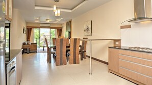 A modern kitchen with a stainless steel range hood, a dining area with wicker chairs, and a view of the outdoors. - Whispering Palms Suite (Koh Samui)