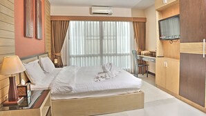 A hotel room with a bed, a desk, a chair, an air conditioning unit, and a television. - Whispering Palms Suite (Koh Samui)