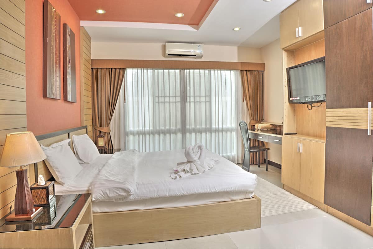 Ein Hotelzimmer mit Bett, Schreibtisch, Stuhl, Klimaanlage und Fernseher.