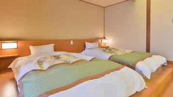 Habitación de hotel con dos camas, cada una con cabecera, lámparas de noche y una mesita entre ellas.