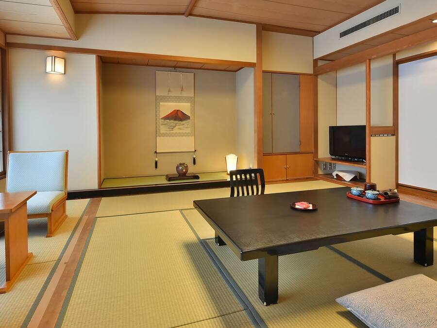 Una habitación tradicional japonesa con suelo de tatami, una mesa baja, sillas de madera, un televisor y puertas correderas.