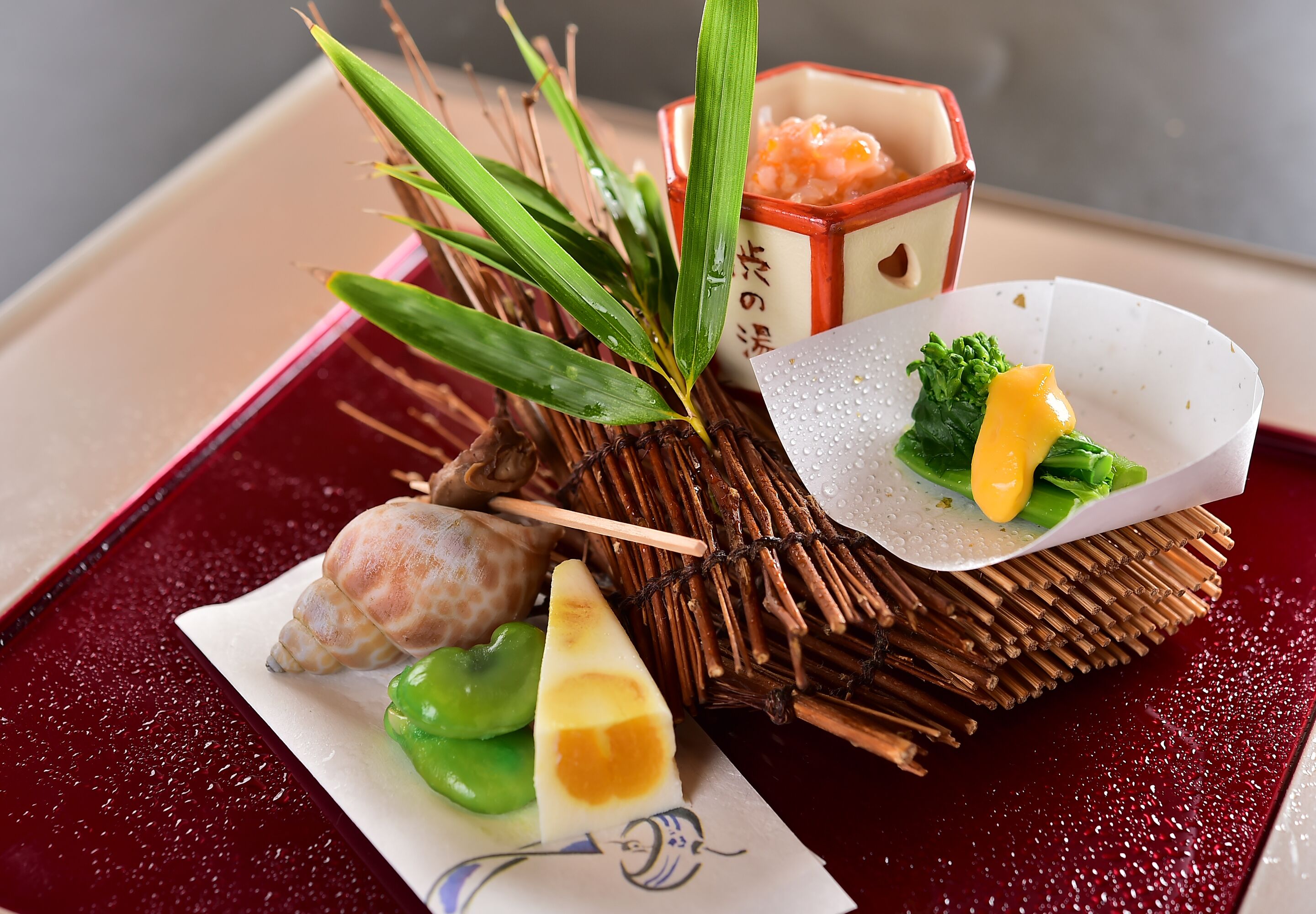 En traditionel japansk servering med en flettet kurv, en lille skål med fiskefor, en skive sashimi og dekorative elementer som en sødskal og grønne blade.