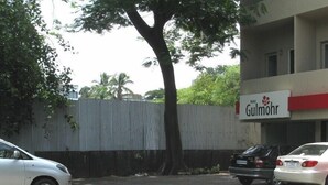 Un área de estacionamiento con un árbol, un edificio con un letrero que dice "Hotel Gulmohor" y una cerca de metal corrugado.