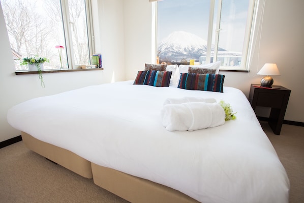 A large bed with white linens, multiple pillows, and a neatly folded towel.