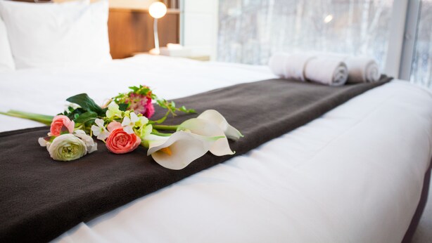 A neatly made bed with a dark bedspread, white pillows, and a bouquet of flowers on the bed.