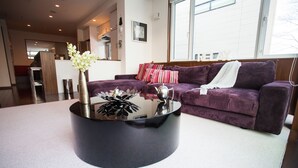 A modern living room with a round black coffee table, a purple sofa with striped cushions, and a white vase with flowers.