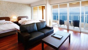 A hotel room with a bed, a sofa, a coffee table, and a balcony with a view of the sea. - Ibusuki Seaside Hotel (Ibusuki)