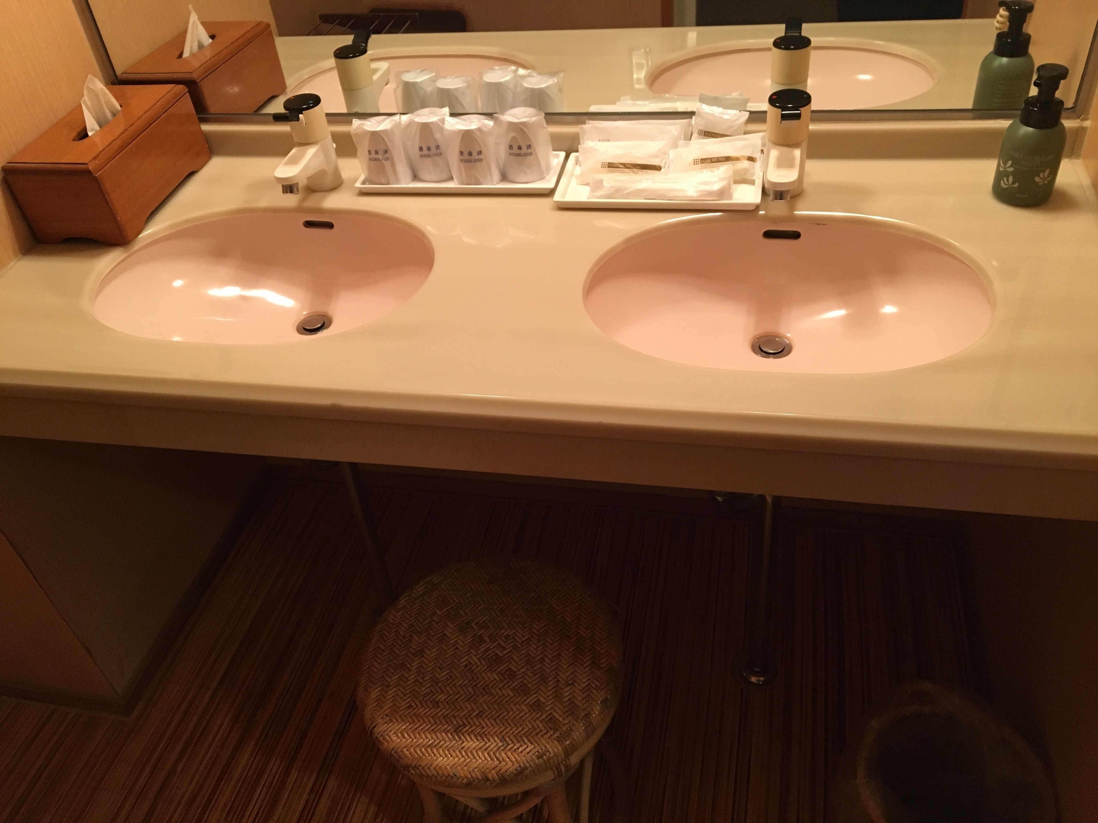 A bathroom with two sinks, a mirror, a tissue box, and a bottle of hand sanitizer.