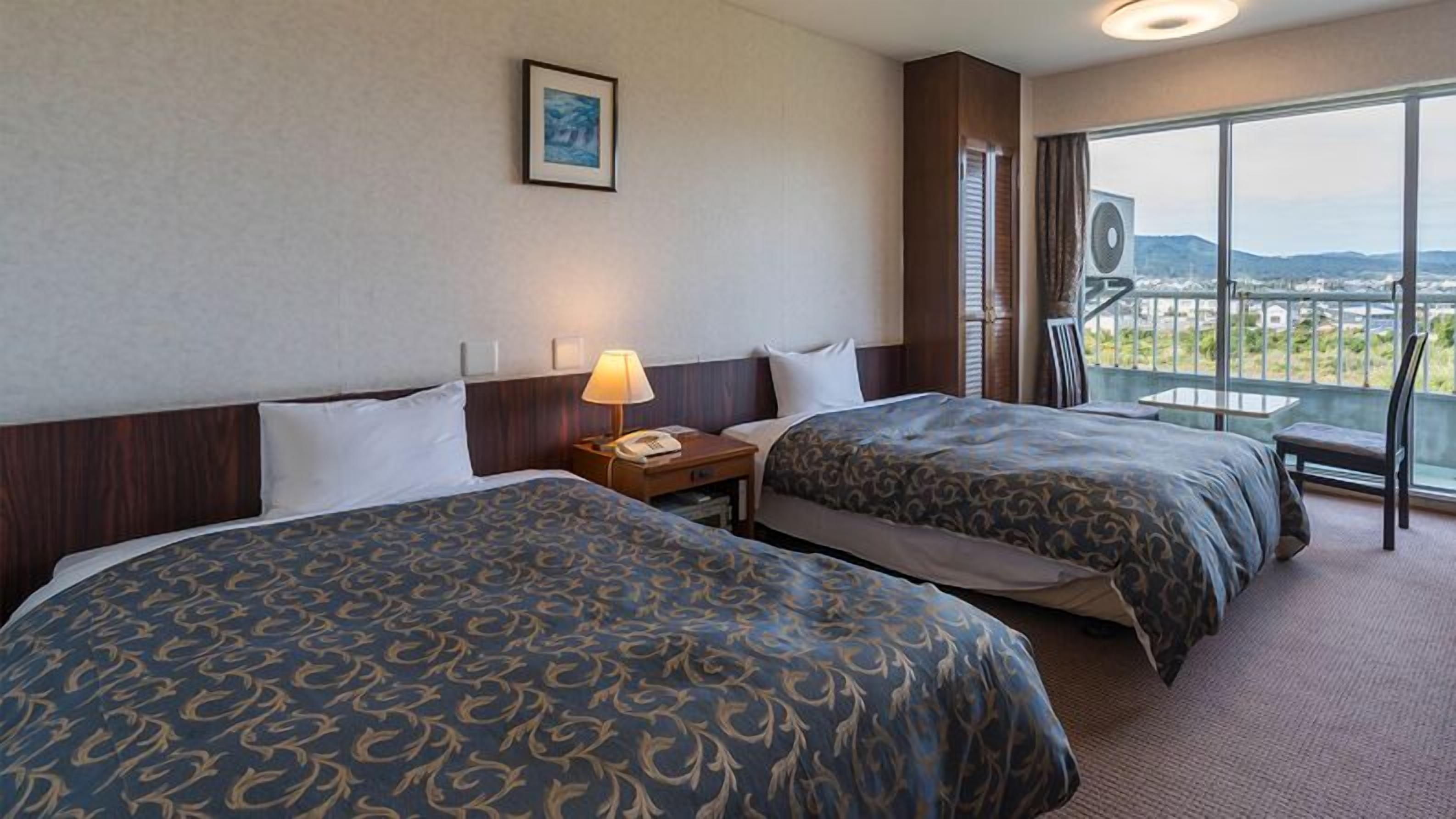 A hotel room with two beds, a nightstand, a lamp, a framed picture on the wall, and a balcony with a view.