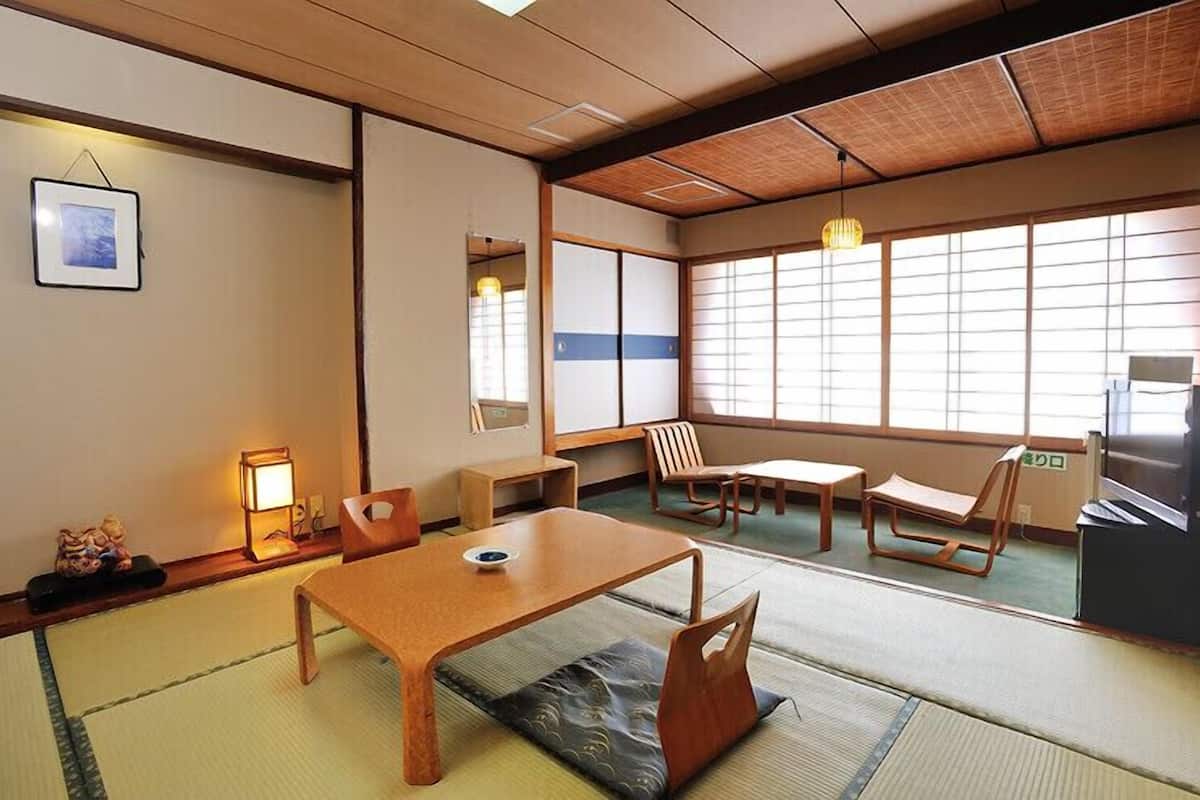 A traditional Japanese room with tatami flooring, a low table, chairs, and a sliding door.