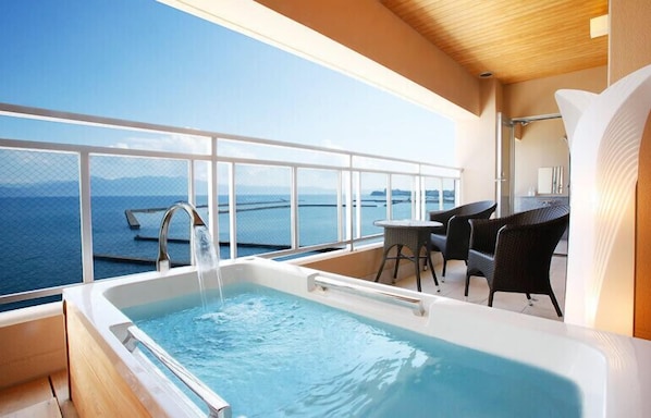A balcony with a hot tub, wicker chairs, and a view of the sea.
