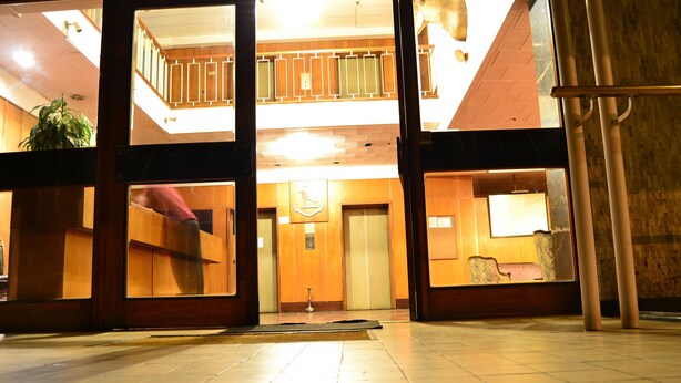 A hotel lobby with a high ceiling, wooden flooring, and a central elevator.