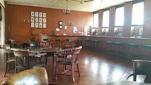 A spacious room with a long counter, multiple bar stools, and several tables and chairs.