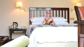 A hotel room with a wooden headboard, a bed with a white and gray striped bedspread, a bedside table with a kettle and a telephone, and a nightstand with a lamp.