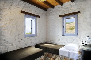 A stone-walled room with two beds, a window, and a soccer ball on a table.