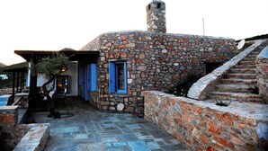 A stone building with a chimney, a blue door, and a staircase leading up. - Aria Villas (Serifos)