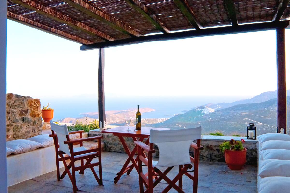 A terrace with a table and chairs, a bottle, and a view of a valley.