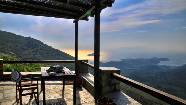 A terrace with a table, chairs, and a view of a coastal landscape. - Aria Villas (Serifos)