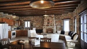 A rustic kitchen with stone walls, wooden beams, and a large hanging light fixture. - Aria Villas (Serifos)